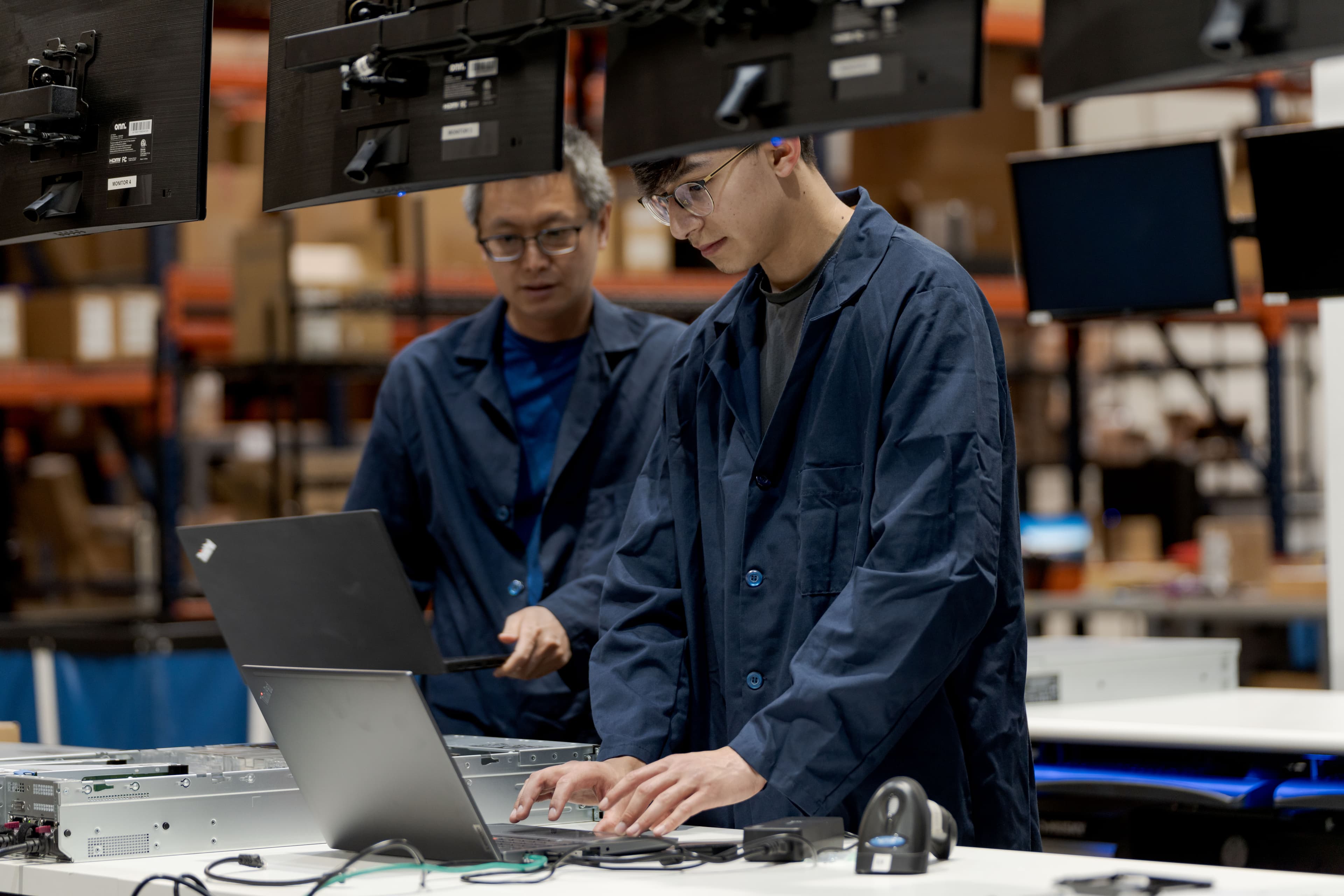Two Fornida technicians in blue lab coats configuring a device at a staging bench