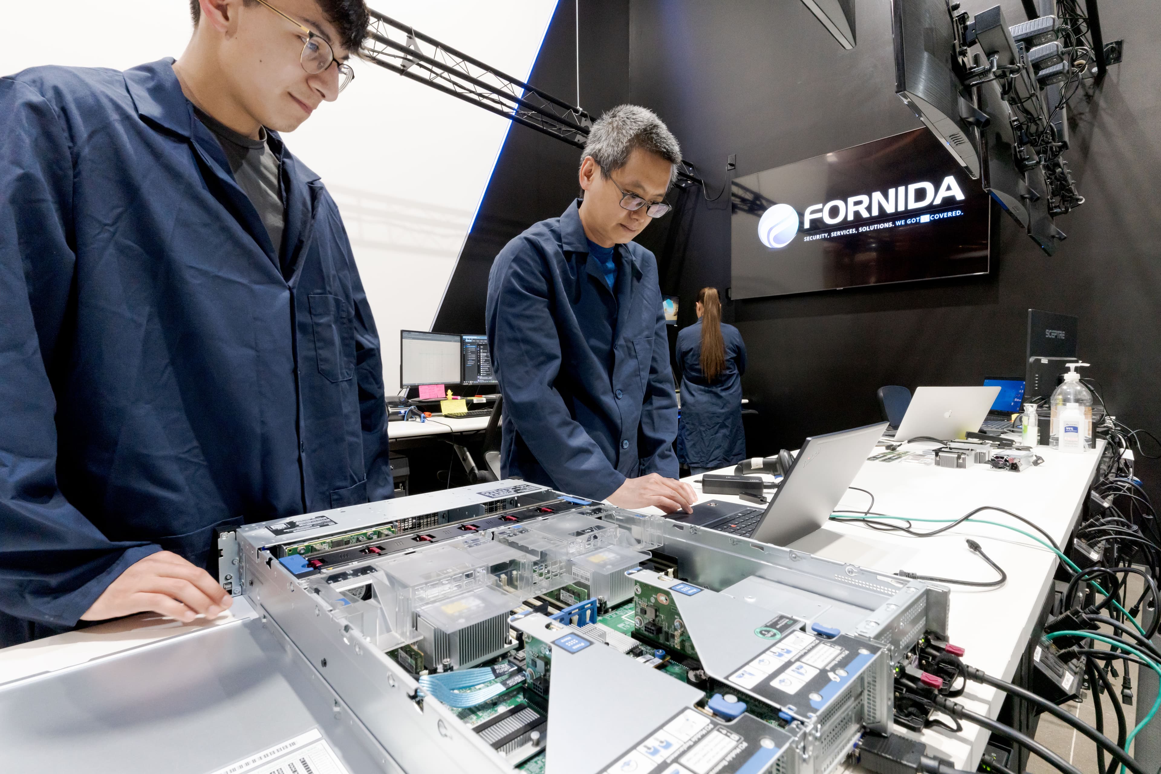 Two Fornida technicians side-by-side at a server bench under the Fornida wall logo